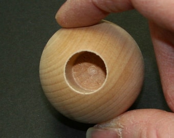 May include: A wooden sphere with a round hole in the center. The sphere is light brown in color and has a smooth surface.