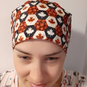 May include: A scrub hat with a geometric pattern of red, white, and black maple leaves.