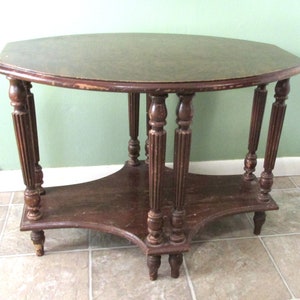 May include: A dark brown wooden oval table with a lower shelf. The table has turned legs with decorative fluting. The table is sitting on a tiled floor.