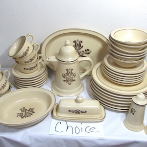 May include: A set of brown and beige stoneware dinnerware with a floral pattern. The set includes a teapot, cups, saucers, bowls, plates, a butter dish, salt and pepper shakers, and a baking dish. The word "Choice" is written on a white card.