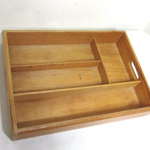 May include: A rectangular wooden cutlery tray with multiple compartments for organizing utensils. The tray is made of light-colored wood and features a handle on one side for easy carrying. The dividers create separate sections for forks, knives, and spoons.
