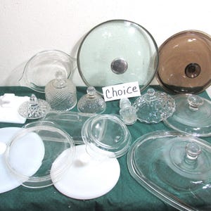 May include: A collection of glass lids and containers, including clear and frosted glass pieces. The assortment features various shapes and sizes, with some lids having knobs. The word "Choice" is written on a white card.