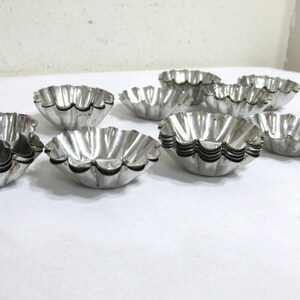 May include: A set of ten silver metal fluted tart pans. The pans are stacked and arranged on a white surface.