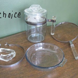 May include: A collection of vintage glass kitchenware, including a coffee pot, pie dish, and a magnifying glass. The coffee pot has a metal band and handle. The word "choice" is written on the upper left.