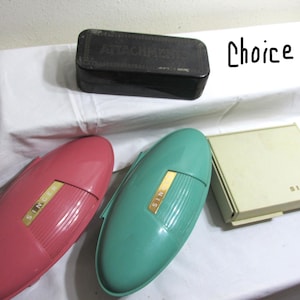 May include: Four vintage Singer sewing machine attachments in various colors. A black rectangular box labeled "Attachment", a teal blue oval case, a pink oval case, and a white rectangular box labeled "Singer".
