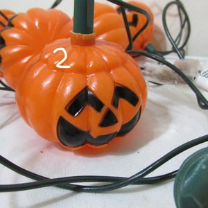 May include: Orange plastic Halloween pumpkin lights with black facial features. The string lights have green stems and black wiring. The pumpkins are a classic decoration for the fall season and Halloween.