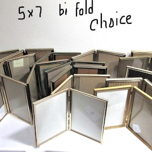 May include: A group of 5x7 bi-fold photo frames in gold metal. The frames are arranged in a semi-circle, with the open frames in the center.