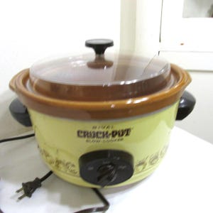 May include: A yellow Rival Crock-Pot slow cooker with a brown rim and lid. The appliance has a black control knob and handles, and a clear lid. The text "Crock-Pot Slow Cooker" is printed on the front.