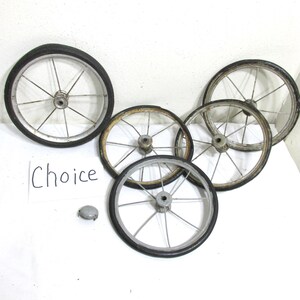 May include: A collection of vintage bicycle wheels with black rubber tires and silver spokes. The wheels are arranged on a white surface, with a small metal cap and a sign that says "Choice".