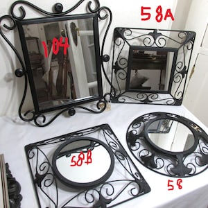 May include: A selection of decorative mirrors with black wrought iron frames. The mirrors are in various shapes, including square and round. The frames have ornate scrollwork and embellishments, giving a vintage look.