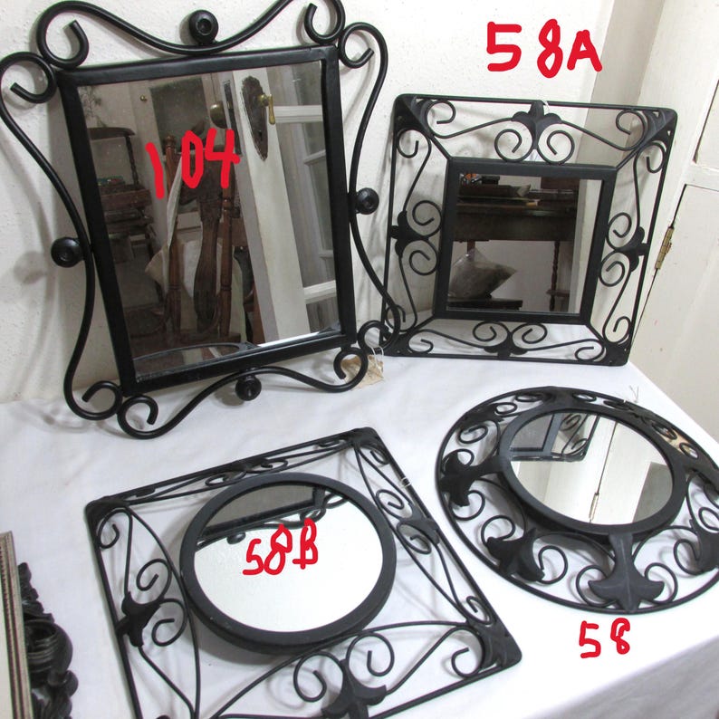 May include: A selection of decorative mirrors with black wrought iron frames. The mirrors are in various shapes, including square and round. The frames have ornate scrollwork and embellishments, giving a vintage look.