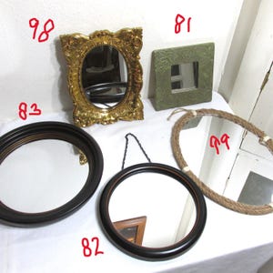 May include: A selection of decorative mirrors in different designs. Features an ornate gold oval mirror, a square green mirror with the word "Inspire", a round black framed mirror, a hanging round mirror, and a rope-framed mirror.