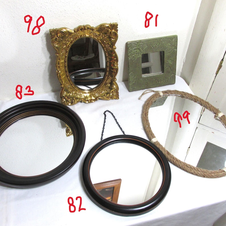 May include: A selection of decorative mirrors in different designs. Features an ornate gold oval mirror, a square green mirror with the word "Inspire", a round black framed mirror, a hanging round mirror, and a rope-framed mirror.