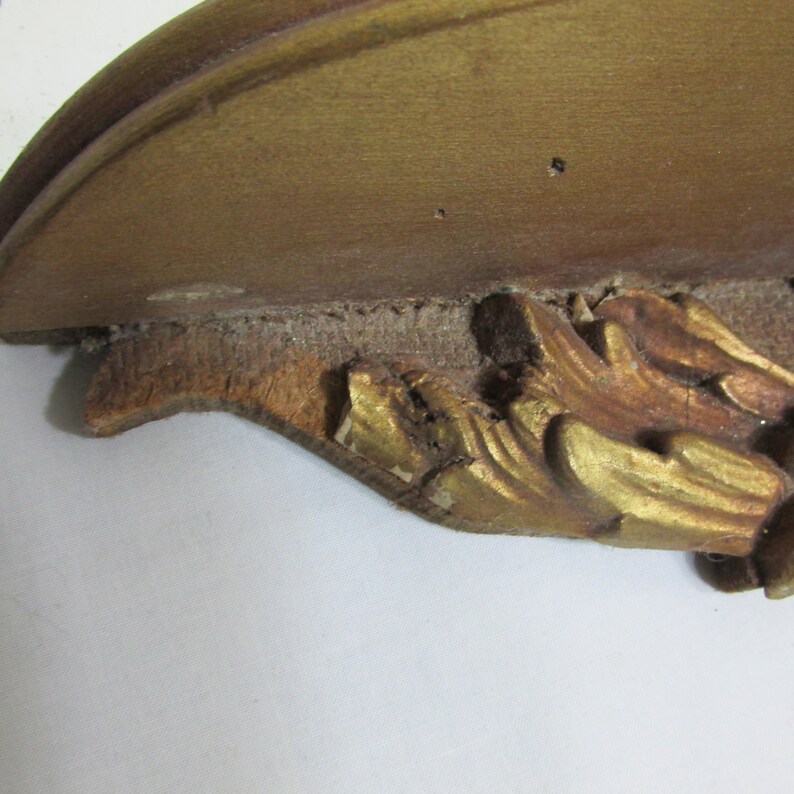 May include: A gold-painted wooden shelf bracket with ornate scrollwork and a chipped edge.
