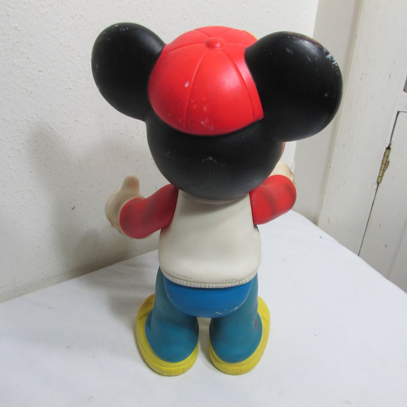 K&ouml;nnte beinhalten: Eine Vintage-Mickey-Mouse-Figur, von hinten gesehen. Die Figur tr&auml;gt eine rote Baseballkappe, ein wei&szlig;es Hemd, blaue Hosen und gelbe Schuhe. Die Ohren sind schwarz und die Arme rot.