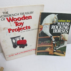 May include: Two instructional books on woodworking. The left book is titled The Workbench Treasury of Wooden Toy Projects for the Home Craftsman and features a red and gray toy train. The right book is titled Making Rocking Horses by Anthony Dew.