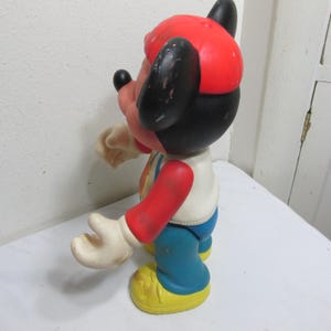 K&ouml;nnte beinhalten: Vintage Mickey Mouse Figur. Die Figur tr&auml;gt eine rote M&uuml;tze, ein wei&szlig;es Hemd mit farbenfrohem Design, rote &Auml;rmel, eine blaue Hose und gelbe Schuhe. Die schwarzen Ohren und das Gesicht sind sichtbar.