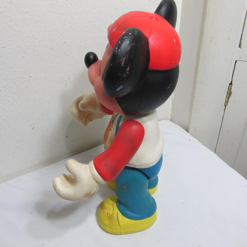 K&ouml;nnte beinhalten: Vintage Mickey Mouse Figur. Die Figur tr&auml;gt eine rote M&uuml;tze, ein wei&szlig;es Hemd mit farbenfrohem Design, rote &Auml;rmel, eine blaue Hose und gelbe Schuhe. Die schwarzen Ohren und das Gesicht sind sichtbar.