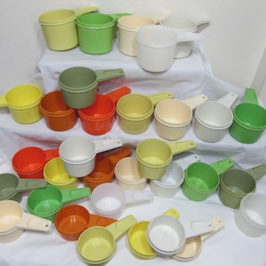 May include: A collection of 24 plastic measuring cups in various colors, including orange, green, yellow, white, and brown. The cups are arranged in a pyramid shape on a white surface.
