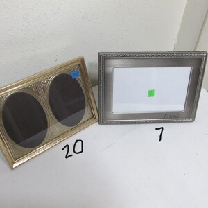 May include: Two picture frames. One is gold-toned with two oval openings. The other is silver-toned with a rectangular opening and the word "Friends" at the bottom. Both frames are empty.