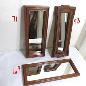 May include: Three wooden framed mirrors. Two are tall and rectangular, and one is a long rectangle. The frames are a medium brown colour. The mirrors reflect the surrounding environment.