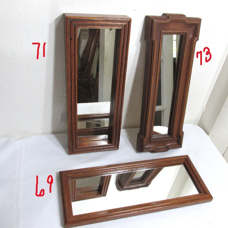 May include: Three wooden framed mirrors. Two are tall and rectangular, and one is a long rectangle. The frames are a medium brown colour. The mirrors reflect the surrounding environment.