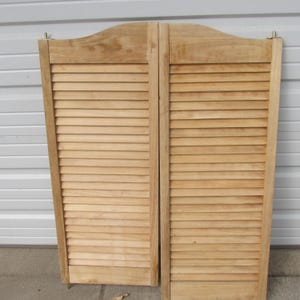 May include: Two wooden saloon doors with horizontal slats. The doors are made of light-colored wood and have a curved top. The doors are hinged and appear to be new or in good condition.