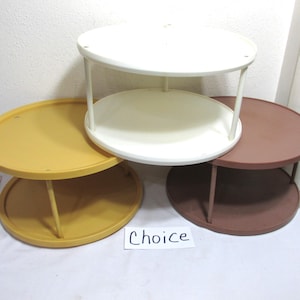 May include: A collection of small, round, two-tiered tables in various colors: white, mustard yellow, and brown. Each table has a circular top and bottom connected by vertical supports. The word "Choice" is written on a small white card.