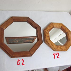 May include: Two octagonal wooden mirrors. The larger mirror has a dark brown frame and reflects a framed picture. The smaller mirror has a lighter oak frame. The number "52" is written in red on the bottom left of the larger mirror, and "72" is written on the bottom right of the smaller mirror.