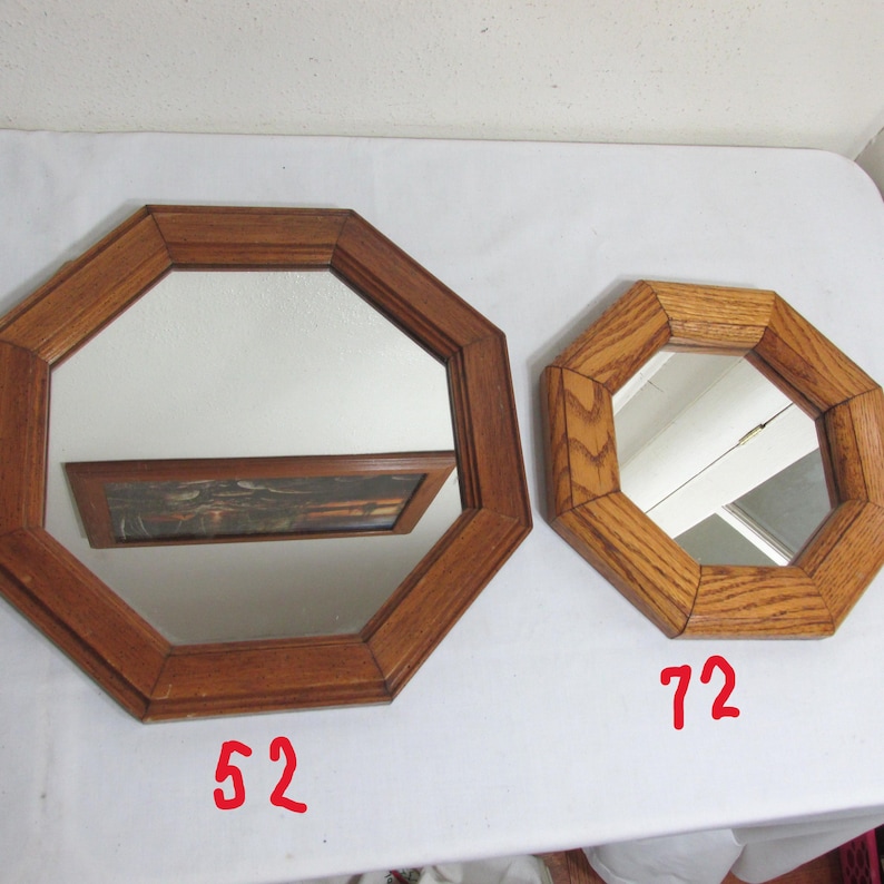 May include: Two octagonal wooden mirrors. The larger mirror has a dark brown frame and reflects a framed picture. The smaller mirror has a lighter oak frame. The number "52" is written in red on the bottom left of the larger mirror, and "72" is written on the bottom right of the smaller mirror.