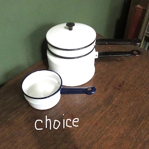 May include: White enamel cookware set with black trim and handles. Includes a small saucepan with a blue handle and a larger pot with a lid. The word "choice" is written in white on the surface.