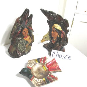 May include: Two ceramic sculptures featuring figures with feathered headdresses, one with a wolf and one with an eagle, alongside a bird-shaped ceramic dish with red, black, and yellow geometric patterns and a small tag labeled Choice.