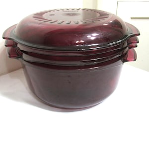 May include: A stack of three burgundy-colored, round food storage containers with lids. The containers have handles and a vented lid design. The containers are made of a transparent material.