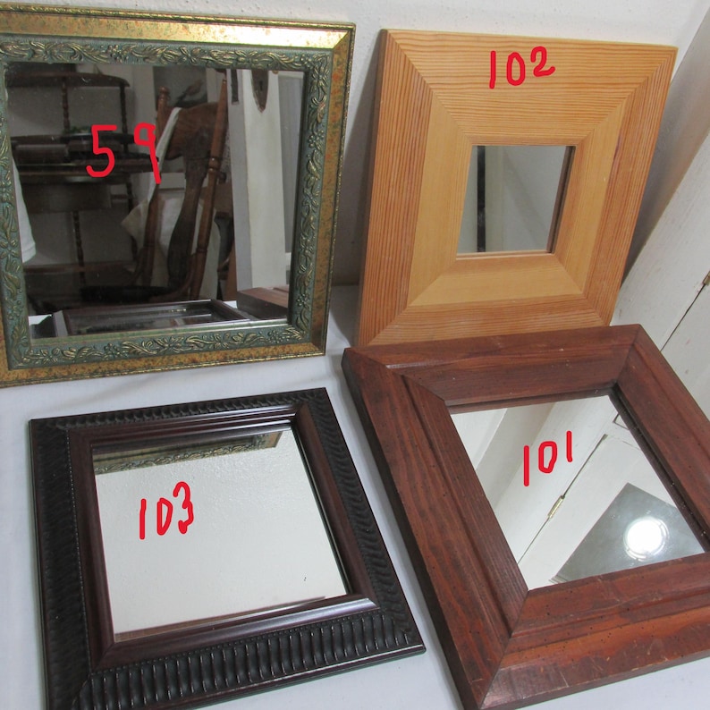 May include: Four square mirrors with various frame designs. One has a gold-coloured frame with floral detailing, another is light wood, and two are dark wood. Each mirror has a number written on it in red.