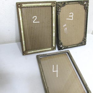 May include: Three antique picture frames with ornate gold-colored metal frames. The frames have different designs, including a rectangular frame with a mother-of-pearl border and two frames with decorative corner details. Numbers 2, 3, and 4 are written on the frames.