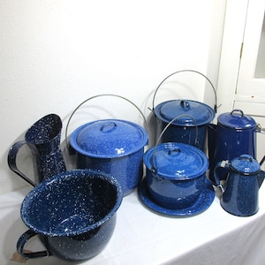 May include: A set of blue enamelware kitchenware, including a pitcher, a large pot, a smaller pot, a coffee pot, and a serving dish. The items are all in a speckled blue enamel finish.