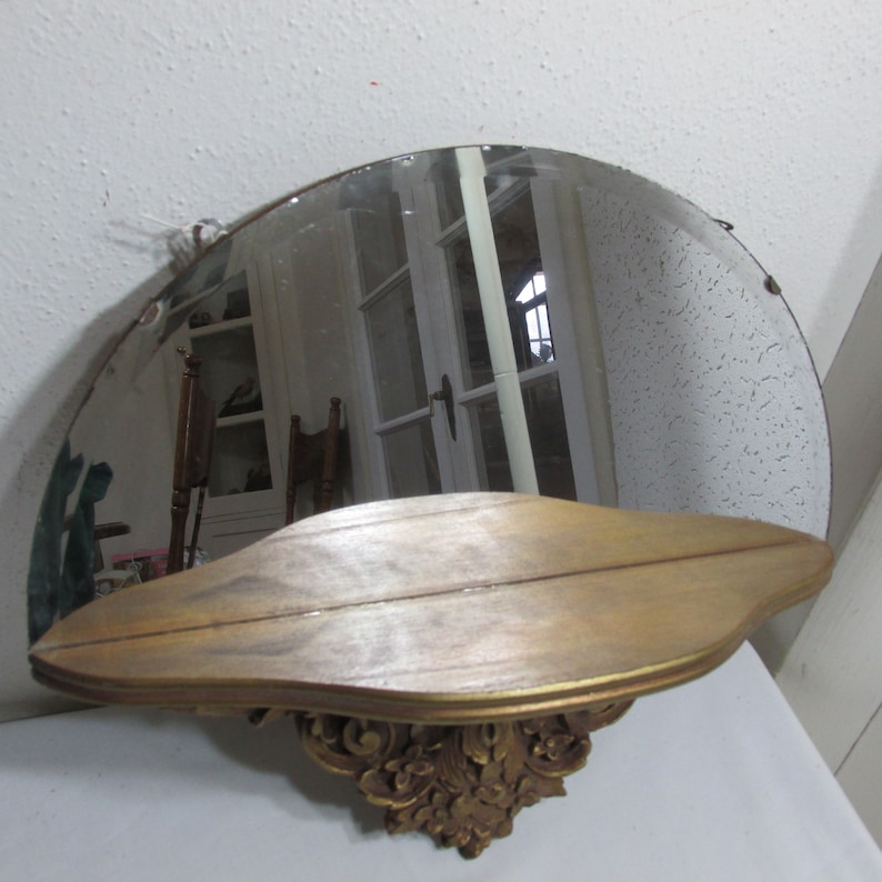 May include: A half-round wall mirror with a gold-painted wooden shelf. The shelf has a carved design and is attached to the bottom of the mirror.