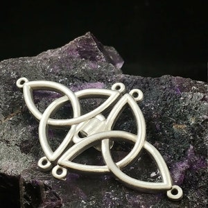 May include: Silver Celtic knot pendant with four loops and a decorative design. The pendant is on a purple and black background.