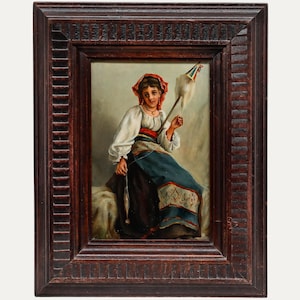 May include: An antique framed painting depicts a woman in traditional attire, seated and spinning yarn. She wears a white blouse, a blue skirt, and a red headscarf. The painting is set in a dark brown, ornate wooden frame.