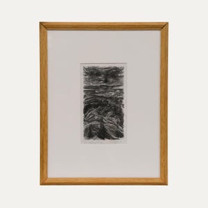 May include: A framed black and white etching featuring a landscape with rolling hills, trees, and a textured sky. The artwork is centered within a white mat board and enclosed in a light-toned wooden frame, displaying a signature and title.