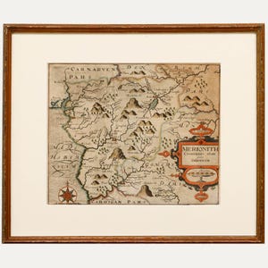 May include: An antique map of Merioneth, a county in Wales, with hand-drawn details and text. The map shows the surrounding counties of Cardigan, Montgomery, Denbigh, and Carnarven. The map is framed in a wooden frame.