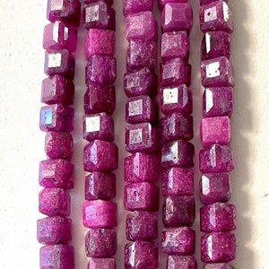 May include: A strand of pink ruby beads, each bead is faceted and has a square shape.