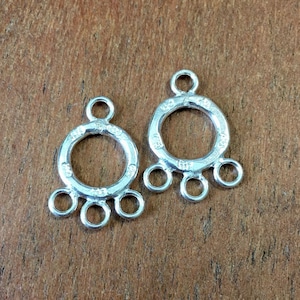 May include: Two silver-toned metal jewelry findings with a round loop and four smaller loops. The findings are designed to connect multiple strands of jewelry.