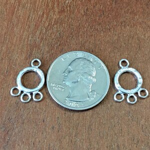 May include: Two silver-toned metal jewelry findings with a circular design and multiple loops. The findings are about the size of a US quarter.