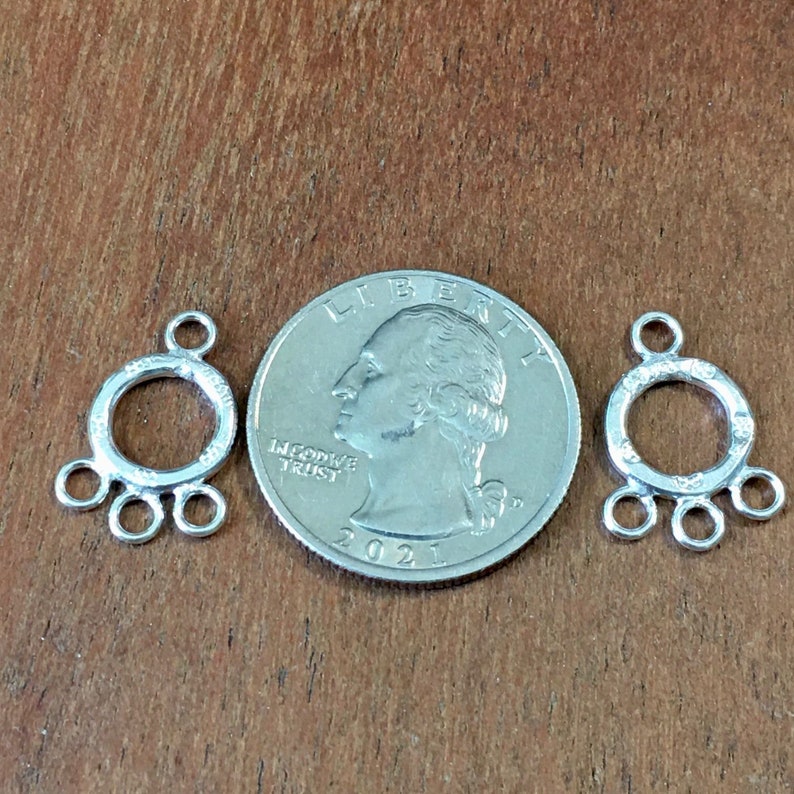 May include: Two silver-toned metal jewelry findings with a circular design and multiple loops. The findings are about the size of a US quarter.