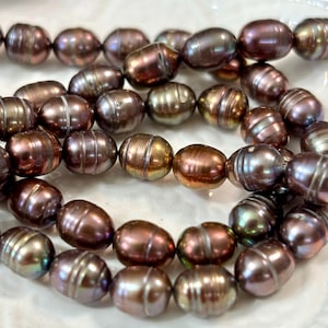 May include: Strands of dark brown freshwater pearls with iridescent hues of gold, green, and purple. The oval-shaped pearls are strung together, showcasing their natural luster and unique surface patterns. These beads are suitable for jewelry making.