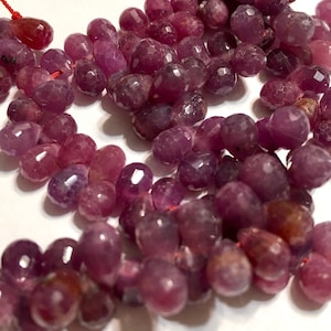 May include: A strand of pink faceted gemstone beads. The beads are teardrop shaped and have a smooth, polished finish.