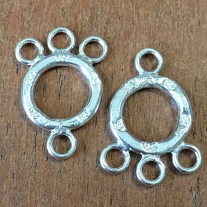 May include: Two silver-toned metal jewelry connectors with three loops each. The connectors have a circular design with a textured surface.
