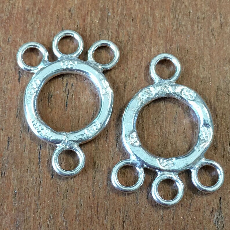 May include: Two silver-toned metal jewelry connectors with three loops each. The connectors have a circular design with a textured surface.