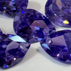 May include: Five purple pear-shaped faceted gemstones with a high shine.